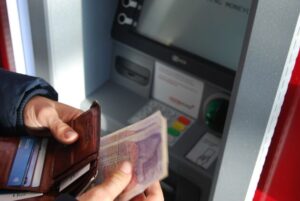 uomo che preleva dei contanti ad un bancomat in Inghilterra primo piano sulle mani che reggono il portafoglio