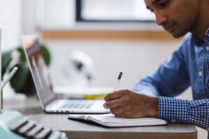Empresário escrevendo anotações em caderno ao lado de um laptop, simbolizando análise fiscal e planejamento de garantias VIES e fianças de IVA.