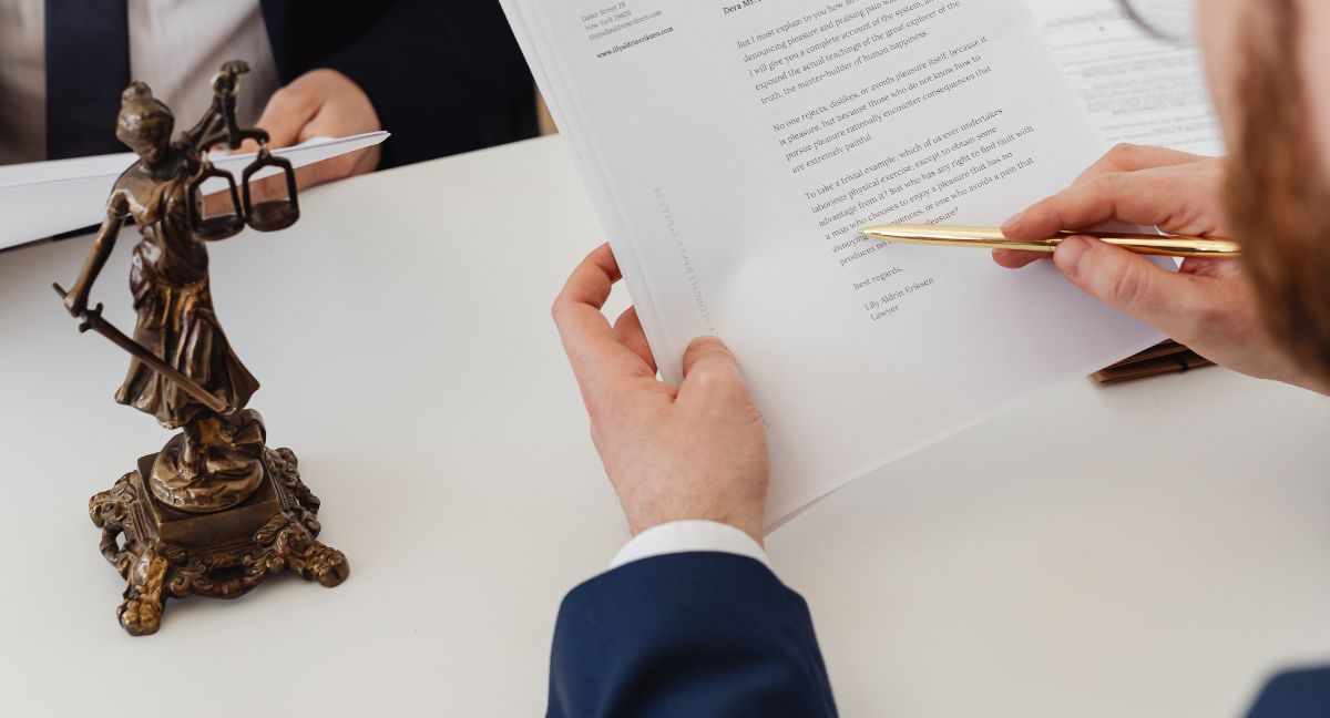 avvocato che analizza un contratto legale con una statua della giustizia sul tavolo