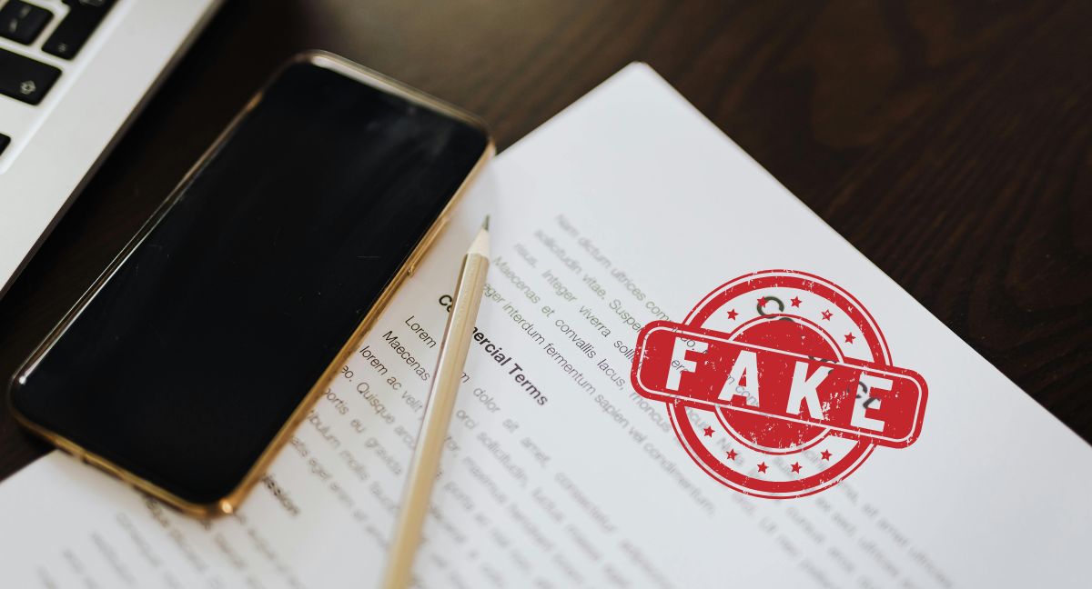 Documento contrattuale con timbro rosso "FAKE", smartphone e parte di laptop. Immagine che simboleggia polizze fideiussorie false e truffe digitali segnalate dall'IVASS.